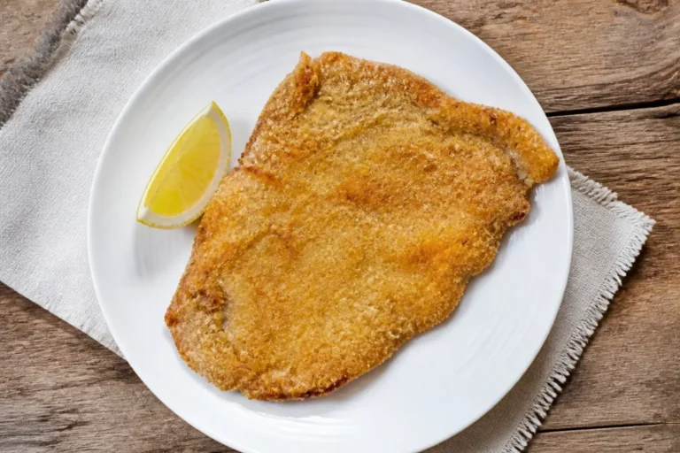 Escalope milanaise panée, dorée et croustillante, posée dans une assiette avec un quartier de citron.